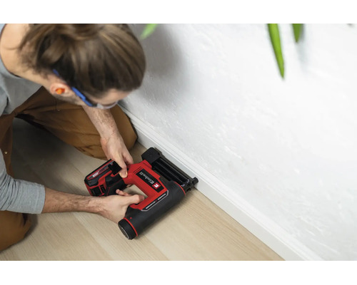 Einhell Akku-Nagler beim Befestigen einer weißen Fußleiste an einer weißen Wand auf hellem Holzboden.