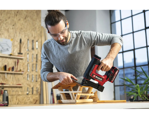 Mann in einer hellen Werkstatt befestigt mit einem Einhell Akku-Nagler Schindeln an einem Vogelhaus aus Holz.