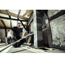 Handwerker schneidet eine Holzleiste mit einer Säbelsäge bei der Sanierung eines Dachstuhls.