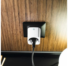 Smarter Zwischenstecker in einer Steckdose auf einer Holzoberfläche mit angeschlossenem Kabel.