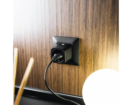 Schwarzer WLAN-Zwischenstecker in einer schwarzen Steckdose an einer Wand in Holzoptik mit eingestecktem Kabel.