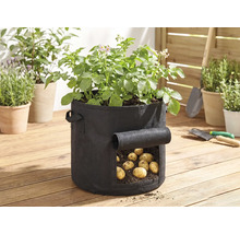 Schwarzer Kartoffel-Pflanzsack aus Textil auf einer Holzterrasse mit Sichtfenster zur Kartoffelernte und grünen Pflanzen.