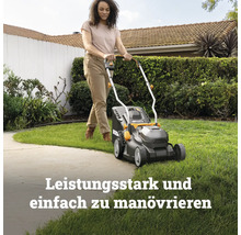 Eine Person mäht mit einem kompakten Rasenmäher eine Rasenfläche in einem sonnigen Garten.