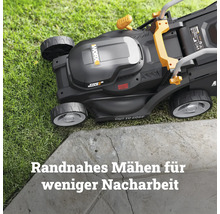 Worx Akku-Rasenmäher mit Cut-to-Edge-Funktion beim randnahen Mähen an einer Steinkante auf einer Rasenfläche.