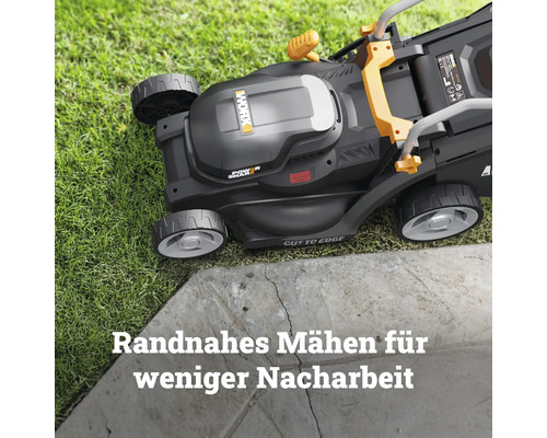 Worx Akku-Rasenmäher mit Cut-to-Edge-Funktion beim randnahen Mähen an einer Steinkante auf einer Rasenfläche.