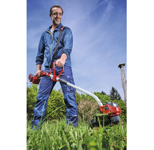 Einhell Akku-Sense im Einsatz: Ein Mann mäht hohes Gras im Garten und trägt dabei Schutzausrüstung sowie einen Tragegurt.