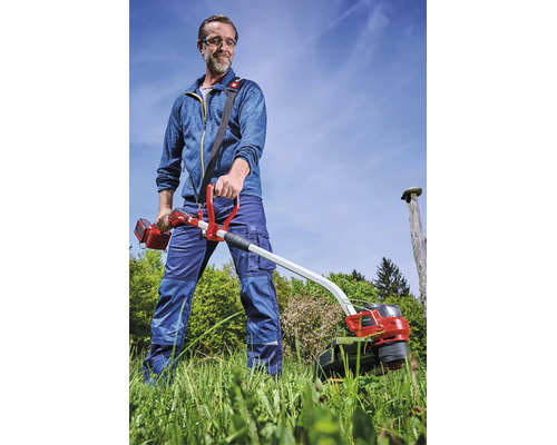 Einhell Akku-Sense im Einsatz: Ein Mann mäht hohes Gras im Garten und trägt dabei Schutzausrüstung sowie einen Tragegurt.