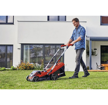 Ein Mann nutzt einen Einhell Akku-Rasenmäher auf einer Rasenfläche vor einem modernen Wohnhaus.