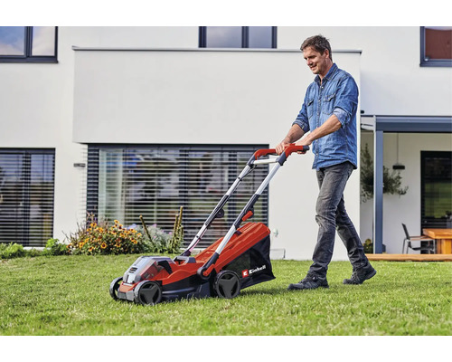 Ein Mann nutzt einen Einhell Akku-Rasenmäher auf einer Rasenfläche vor einem modernen Wohnhaus.