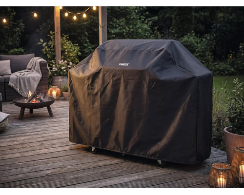 Tenneker Grillabdeckung auf einer hölzernen Terrasse neben einer brennenden Feuerschale und Gartenmöbeln bei Dämmerung im Außenbereich.