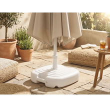 Weißer Sonnenschirmständer aus Kunststoff auf einer gepflasterten Terrasse mit Pflanzen und Sitzkissen.