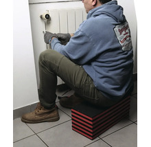 Mann sitzt auf einer rot-schwarz gestreiften modularen Knie- und Sitzmatte bei der Arbeit an einem Heizkörper.