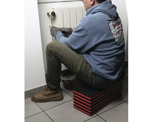 Mann sitzt auf einer rot-schwarz gestreiften modularen Knie- und Sitzmatte bei der Arbeit an einem Heizkörper.