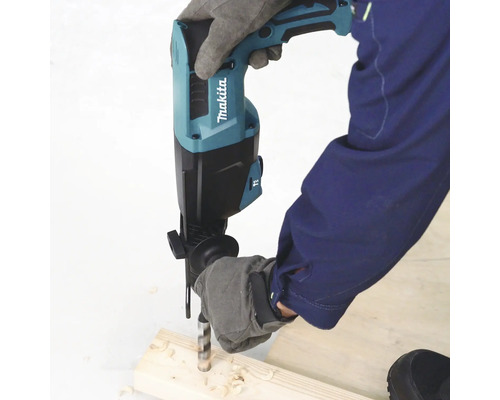 Eine Person mit Schutzhandschuhen bohrt mit einem Makita Bohrhammer in ein Stück Holz. Makita Logo sichtbar.