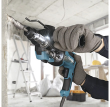 Makita Bohrhammer beim Bohren in Beton auf einer hellen Baustelle, gehalten von einer Person mit Arbeitshandschuhen.