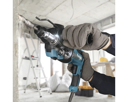 Makita Bohrhammer beim Bohren in Beton auf einer hellen Baustelle, gehalten von einer Person mit Arbeitshandschuhen.