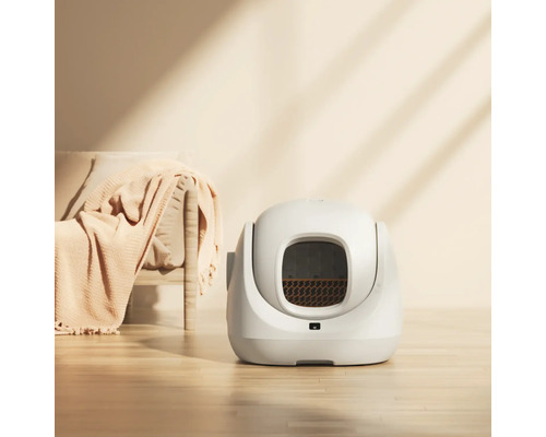 Moderne selbstreinigende automatische Katzentoilette in einem hellen Raum mit Holzboden und Sofa.