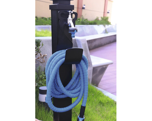 Schwarze Gartenzapfstelle mit silbernem Wasserhahn und einem aufgerollten blauen Gartenschlauch an einer Halterung im Außenbereich.
