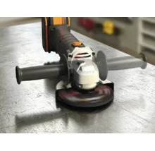 Akku-Winkelschleifer mit Seitengriff und Schleifscheibe auf einer metallischen Arbeitsfläche.