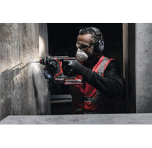 Handwerker bohrt mit Einhell Akku-Bohrhammer in eine Betonwand, trägt Gehörschutz, Schutzbrille und Atemschutzmaske.