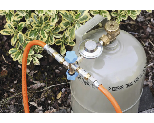 Gasflasche mit Druckregler, Zweifach-Abzweigventil mit Griffen und zwei angeschlossenen Gasschläuchen im Außenbereich.