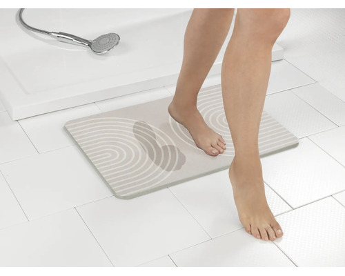 Saugfähige Badmatte aus Kieselgur mit Zen-Muster und sichtbarem Fußabdruck, eine Person tritt barfuß im hellen Badezimmer auf die Matte.