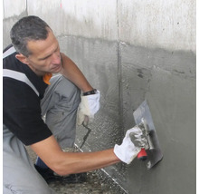 Handwerker trägt mineralische Dichtungsschlämme mit einer Glättekelle auf eine Betonwand auf.