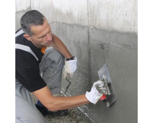 Handwerker trägt mineralische Dichtungsschlämme mit einer Glättekelle auf eine Betonwand auf.
