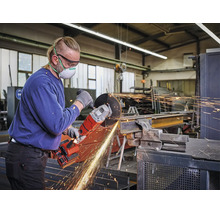 Handwerker nutzt einen Akku-Winkelschleifer zur Metallbearbeitung in einer Werkstatt, sichtbarer Funkenflug.