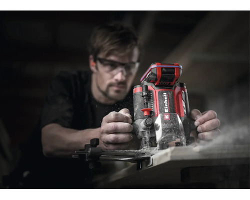 Einhell Akku-Oberfräse bei der Holzbearbeitung durch eine Person mit Schutzbrille in einer Werkstatt.