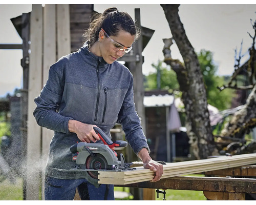 Eine Frau schneidet im Freien ein Holzbrett mit einer Einhell Handkreissäge und trägt Schutzbrille sowie Gehörschutz.