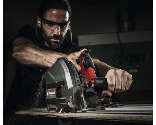 Ein Mann verwendet eine Einhell Tauchkreissäge mit Führungsschiene zum Schneiden von Holz, trägt Schutzbrille und Gehörschutz.