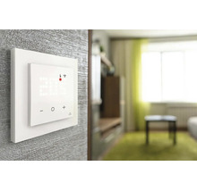 Smartes Wandthermostat mit Digitalanzeige für Temperatur und WLAN-Verbindung sowie Touch-Bedienung in einem hellen Wohnzimmer montiert.