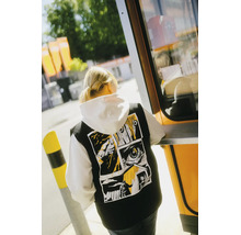 Schwarze Weste mit Comic-Grafikprint auf dem Rücken, getragen über einem weißen Kapuzenpullover.