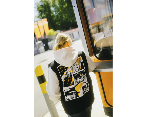 Schwarze Weste mit Comic-Grafikprint auf dem Rücken, getragen über einem weißen Kapuzenpullover.
