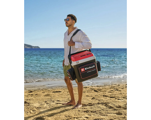 Ein Mann trägt eine Einhell Kühltasche mit Schultergurt und Seitentaschen an einem hellen Sandstrand am Meer. Einhell Logo.
