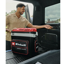Tragbare Einhell Kühlbox mit Zubehörtasche, die im Kofferraum eines Autos an eine 12-Volt-Steckdose angeschlossen wird.
