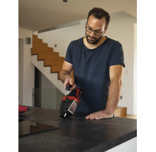 Ein Mann reinigt mit einem Handstaubsauger von Einhell Kaffeebohnen von einer Küchenarbeitsplatte in einem modernen, hellen Wohnraum.
