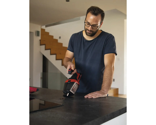 Ein Mann reinigt mit einem Handstaubsauger von Einhell Kaffeebohnen von einer Küchenarbeitsplatte in einem modernen, hellen Wohnraum.
