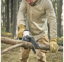 Eine Person mit Schutzhandschuhen schneidet mit einer kompakten Akku-Kettensäge einen Ast in einem Wald.