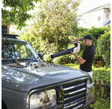 Ein Mann verwendet einen Litheli Akku-Laubbläser, um Blätter von der Motorhaube eines grauen Autos im Garten zu entfernen.