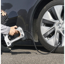 Eine Person verwendet einen tragbaren elektrischen Luftkompressor, um einen Autoreifen aufzupumpen.