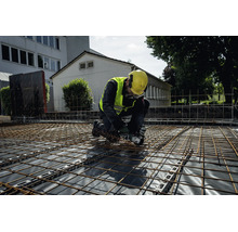 Ein Bauarbeiter mit Schutzausrüstung bearbeitet Bewehrungsmatten mit einem Metabo Akku-Winkelschleifer auf einer Baustelle.