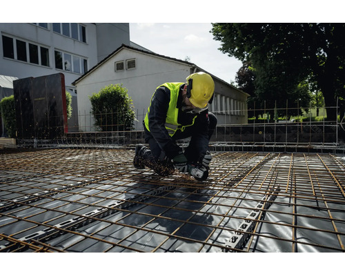 Ein Bauarbeiter mit Schutzausrüstung bearbeitet Bewehrungsmatten mit einem Metabo Akku-Winkelschleifer auf einer Baustelle.