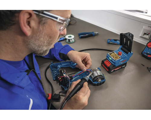 Handwerker lötet mit einem Bosch Akku Lötkolben an einem geöffneten Elektrowerkzeug an einem Werkstatttisch.
