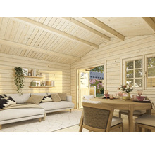 Innenansicht eines hellen Gartenhauses aus Holz mit Wohnbereich, Sofa, Esstisch und Blick in den Garten durch Tür und Fenster.