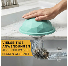 Türkisfarbenes Abfluss-Sieb mit Facetten-Design auf einem Waschbecken. Ein Querschnitt zeigt im Siphon aufgefangene Haare bei fließendem Wasser.