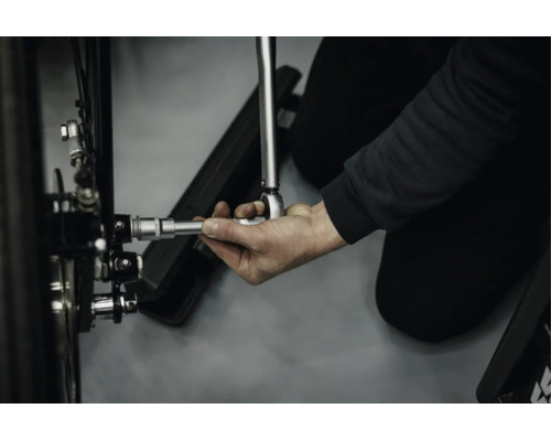 Eine Hand bedient einen Drehmomentschlüssel mit Verlängerung an einer Fahrradnabe.