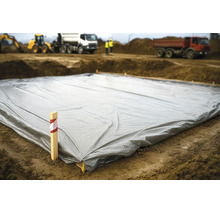 Eine große graue Baufolie auf dem Boden einer Baustelle mit Baumaschinen und Arbeitern im Hintergrund.