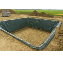 Eine quadratische Baugrube, die mit einer dunkelgrünen PE-Folie ausgekleidet ist, auf einer Baustelle mit Erdhaufen im Hintergrund.